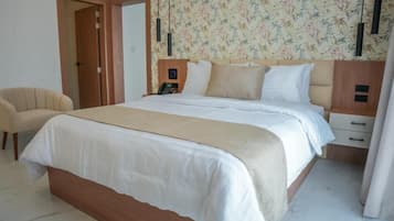 Un dormitorio con cama, mesitas de noche, una silla y una puerta.