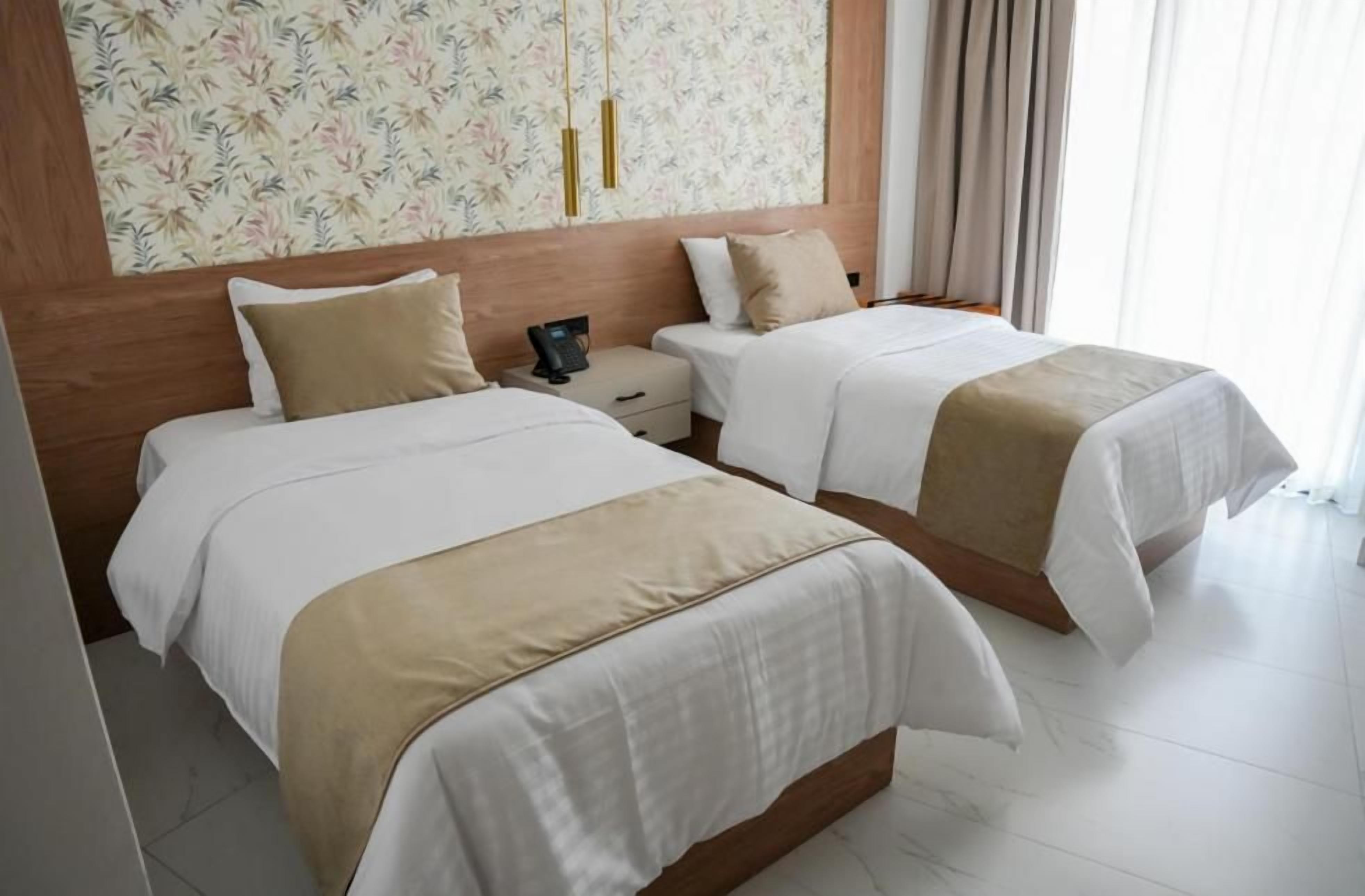 A hotel room with two beds, a wooden headboard, a nightstand, and a floral-patterned wall.