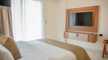 Habitación de hotel con cama, televisor montado en la pared y ventana con cortinas.