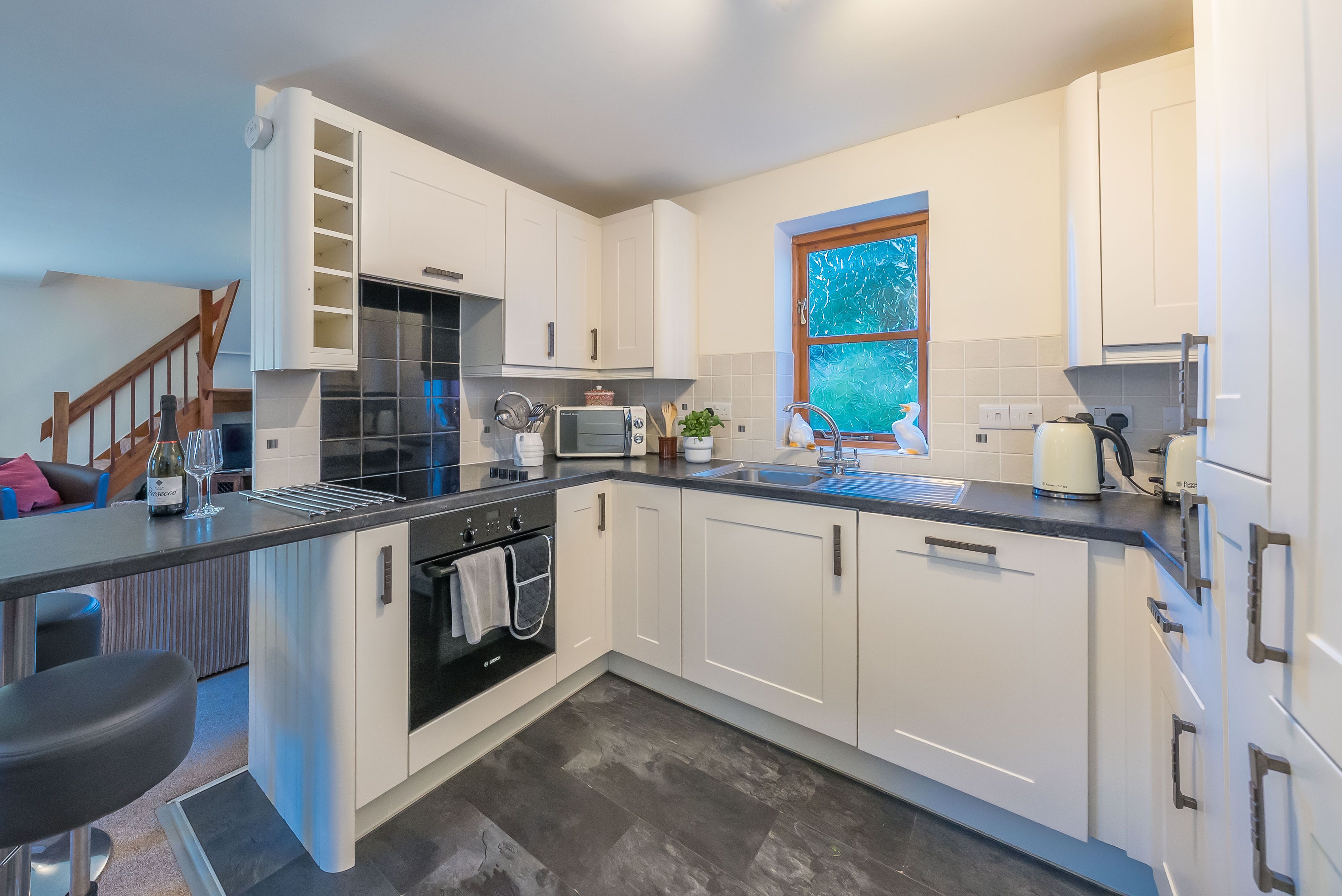 A modern kitchen with white cabinetry, a built-in oven, a microwave, and a window with a view.