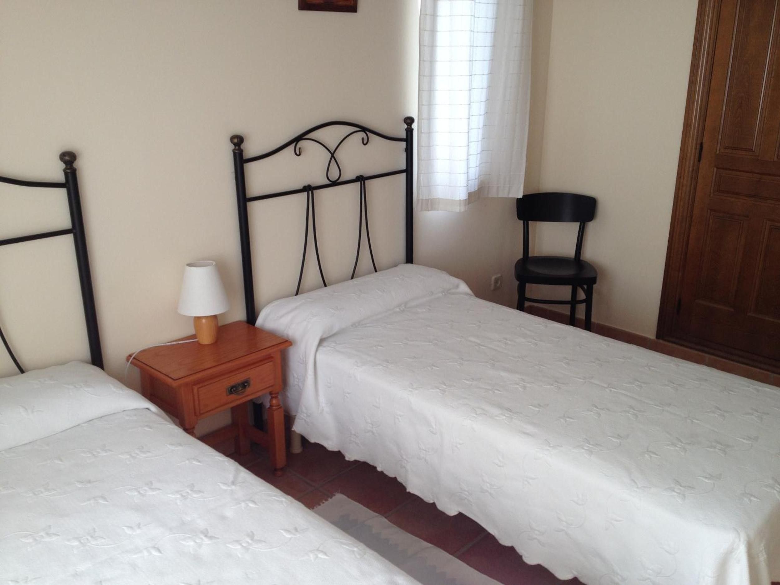A bedroom with two single beds, a nightstand with a lamp, a chair, and a wooden door.