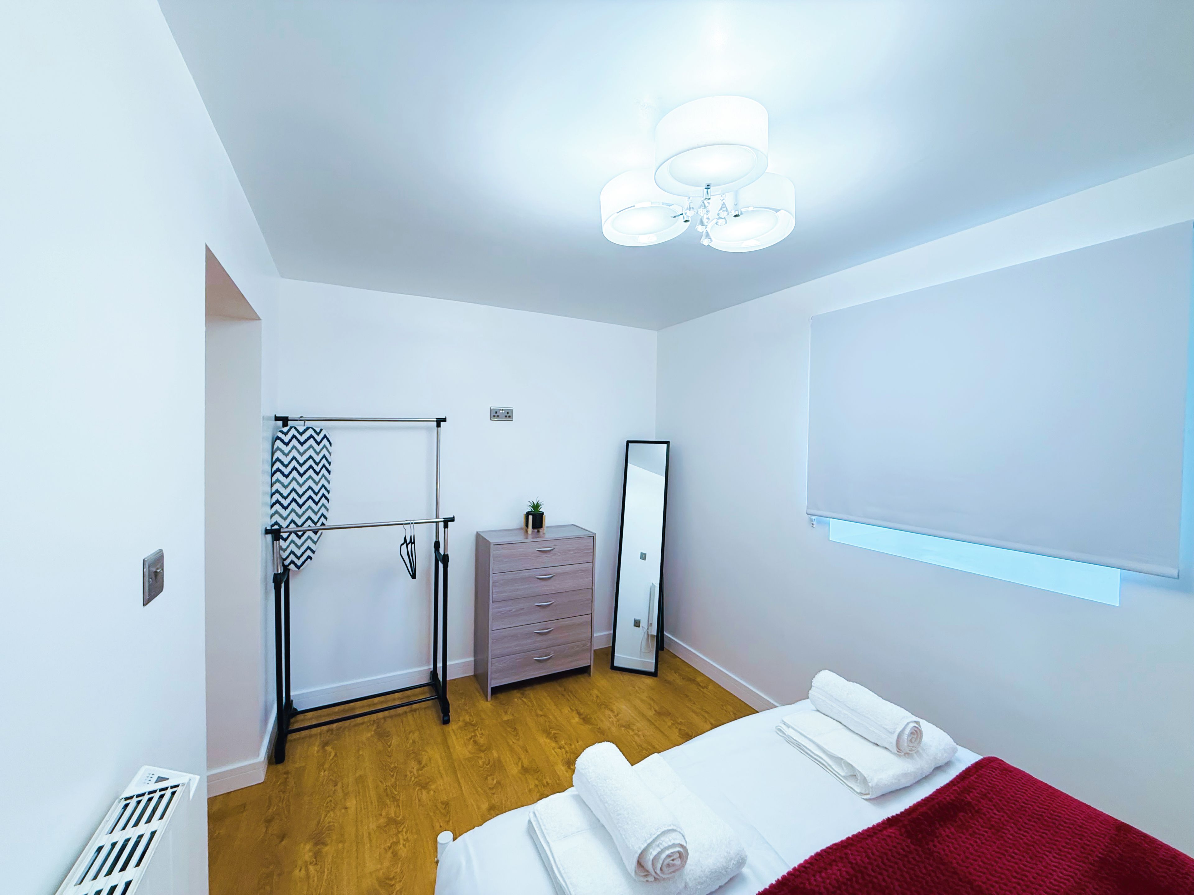 Habitación de hotel con cama, espejo, cómoda, toallero e iluminación en el techo.
