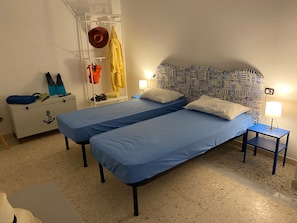A room with two single beds, a white wardrobe, a small table, and a wall with nautical-themed wallpaper.