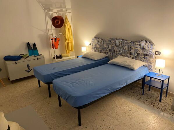 Ein Zimmer mit zwei Einzelbetten, einem weißen Kleiderschrank, einem kleinen Tisch und einer Wand mit Seebildern.