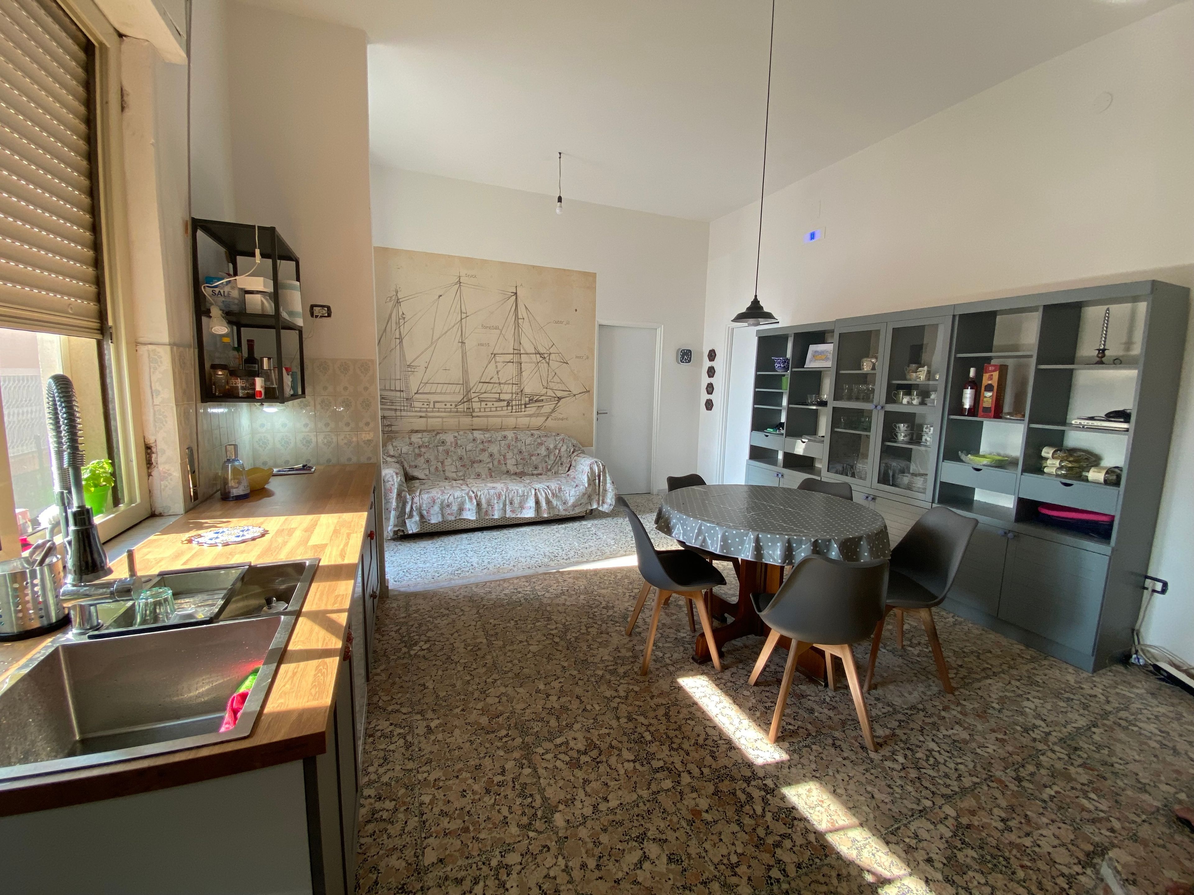 Eine kompakte Küche mit Spüle, einem Esstisch mit Stühlen, einer Couch und einem Schrank mit Glastüren.