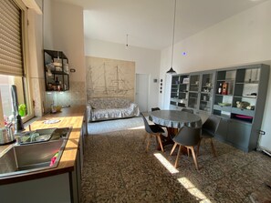 A compact kitchen with a sink, a dining table with chairs, a sofa, and a cabinet with glass doors.