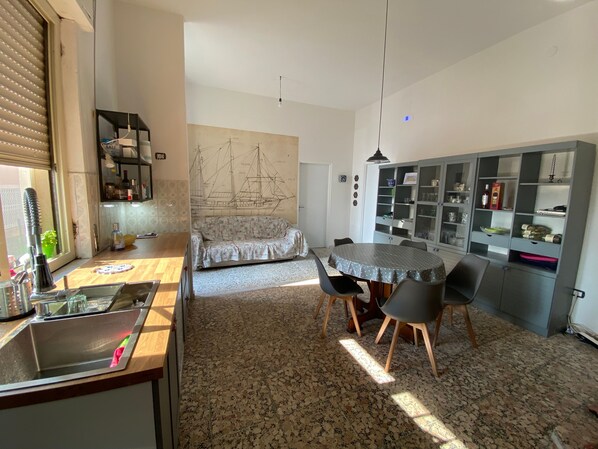 A compact kitchen with a sink, a dining table with chairs, a sofa, and a cabinet with glass doors.