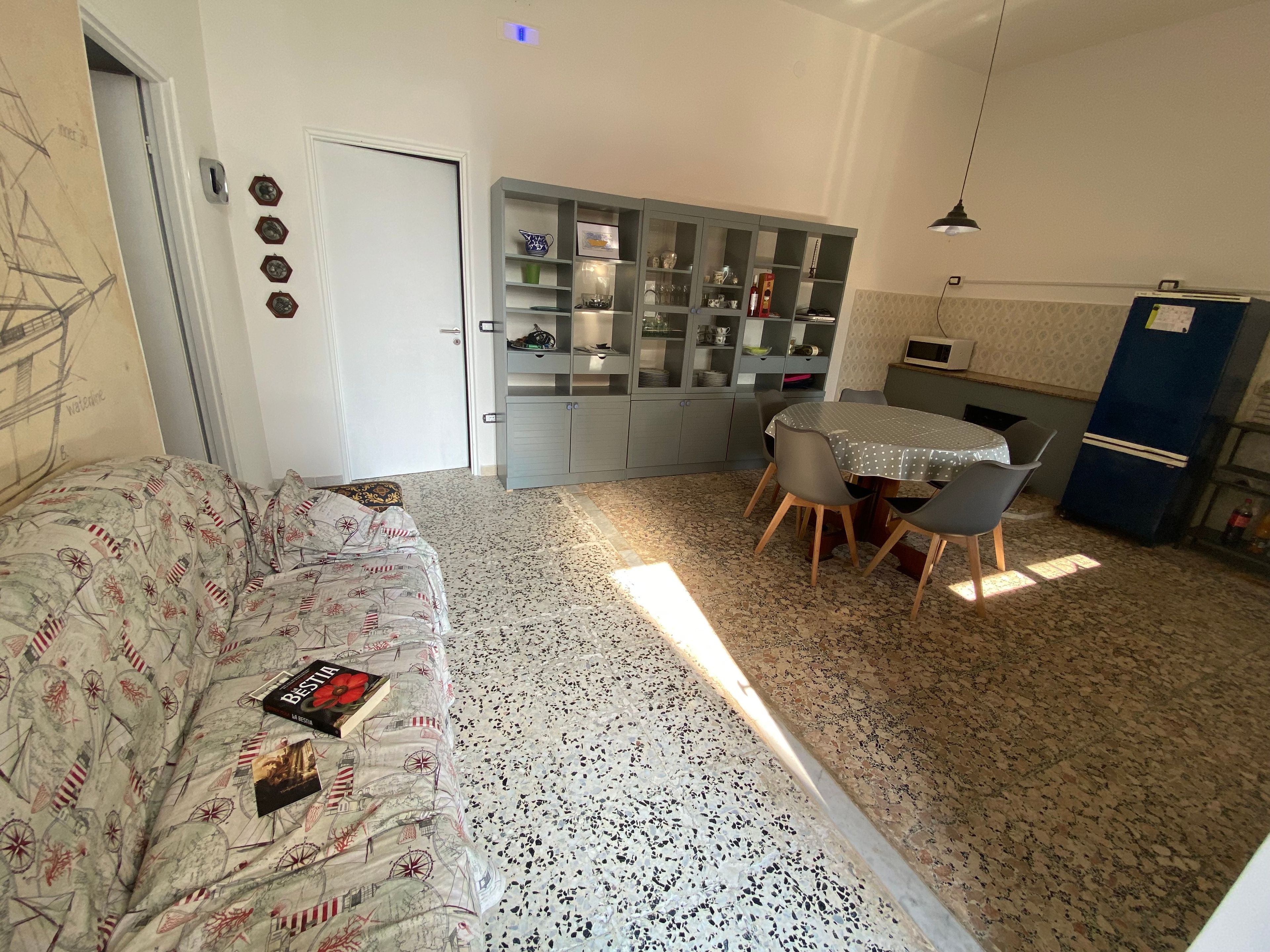 Ein kompakter Wohnbereich mit einer Couch, einem Esstisch mit Stühlen, einer Küchenzeile und einem Schrank mit Glastüren.