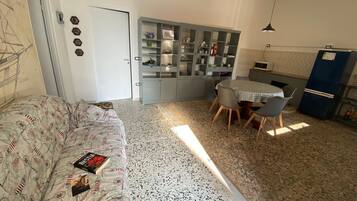 Ein kompakter Wohnbereich mit einer Couch, einem Esstisch mit Stühlen, einer Küchenzeile und einem Schrank mit Glastüren.