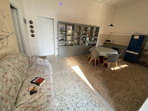 A compact living space with a sofa, a dining table with chairs, a kitchenette, and a cabinet with glass doors.