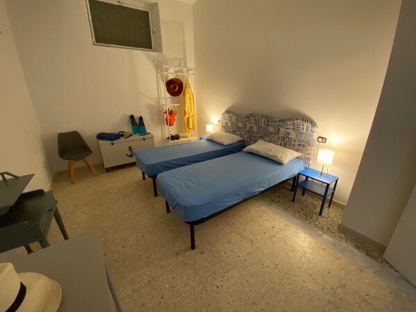 A bedroom with two beds, a desk, a chair, a wardrobe, and a window.