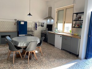Eine kleine Küche mit rundem Tisch, Stühlen, einem Geschirrspüler und einem Fenster mit Jalousien.