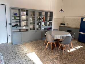 A kitchen with a dining table and chairs, a cabinet with glass doors, and a microwave on the wall.