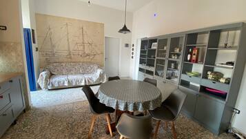 A dining area with a round table, chairs, a patterned sofa, and a wall with a ship illustration.