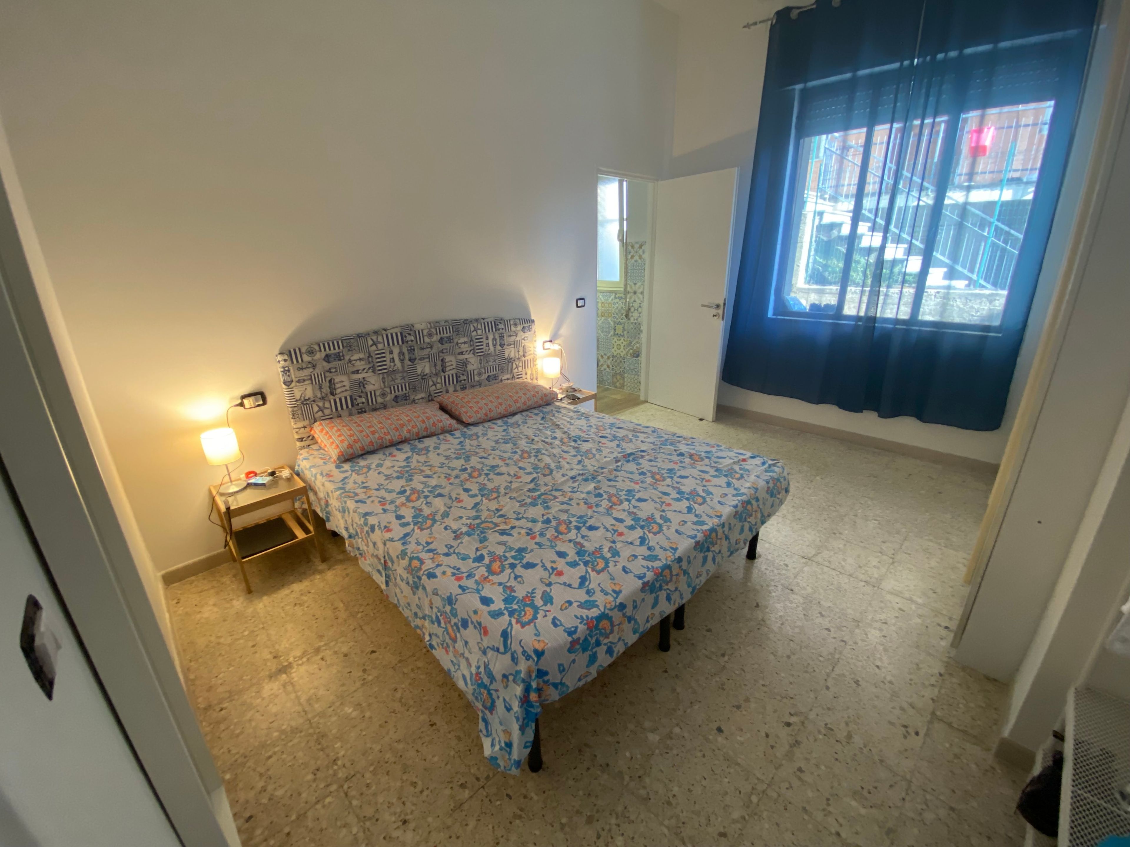 Una camera da letto con un letto, lampade da comodino, una porta e una finestra con tende.