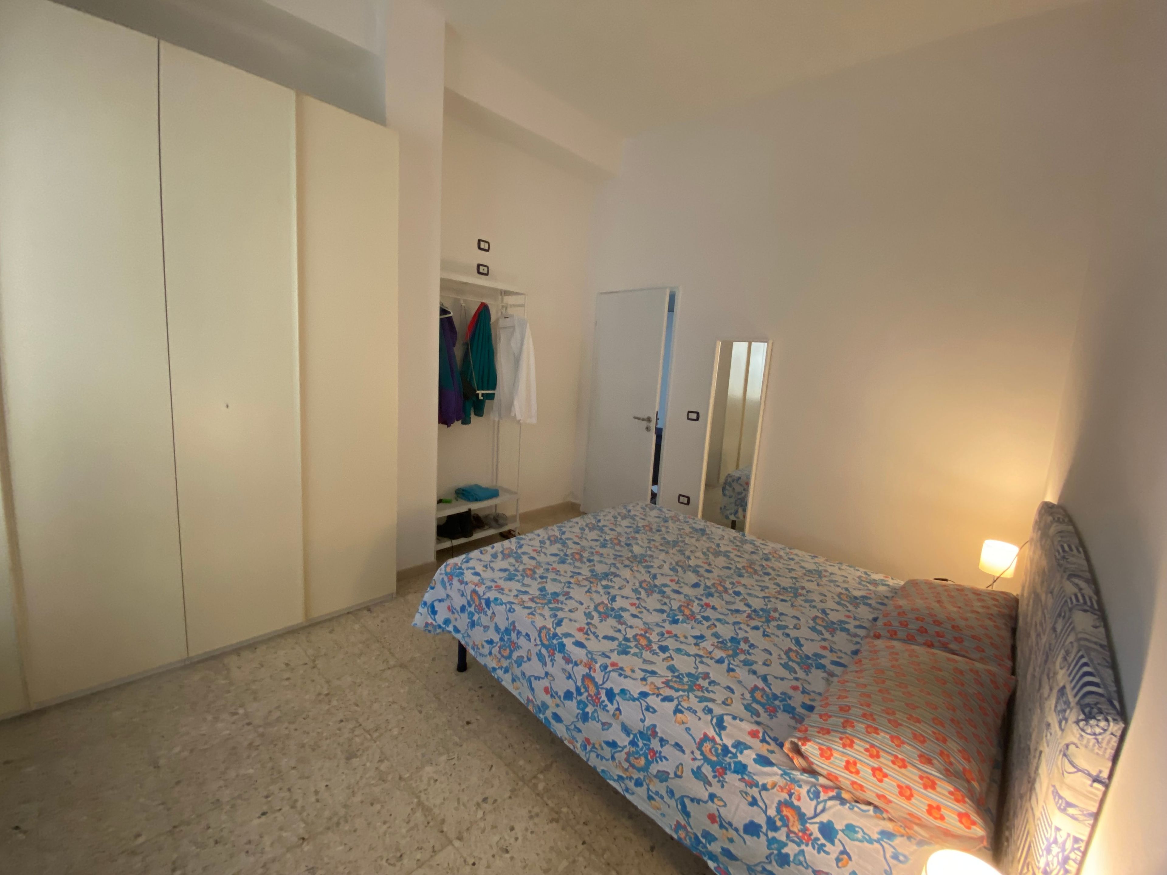 Ein Schlafzimmer mit Bett, Kleiderschrank, Spiegel und Tür.