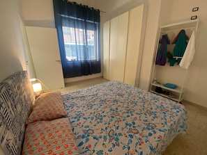 A bedroom with a bed, a wardrobe, a window with curtains, and a bedside lamp.