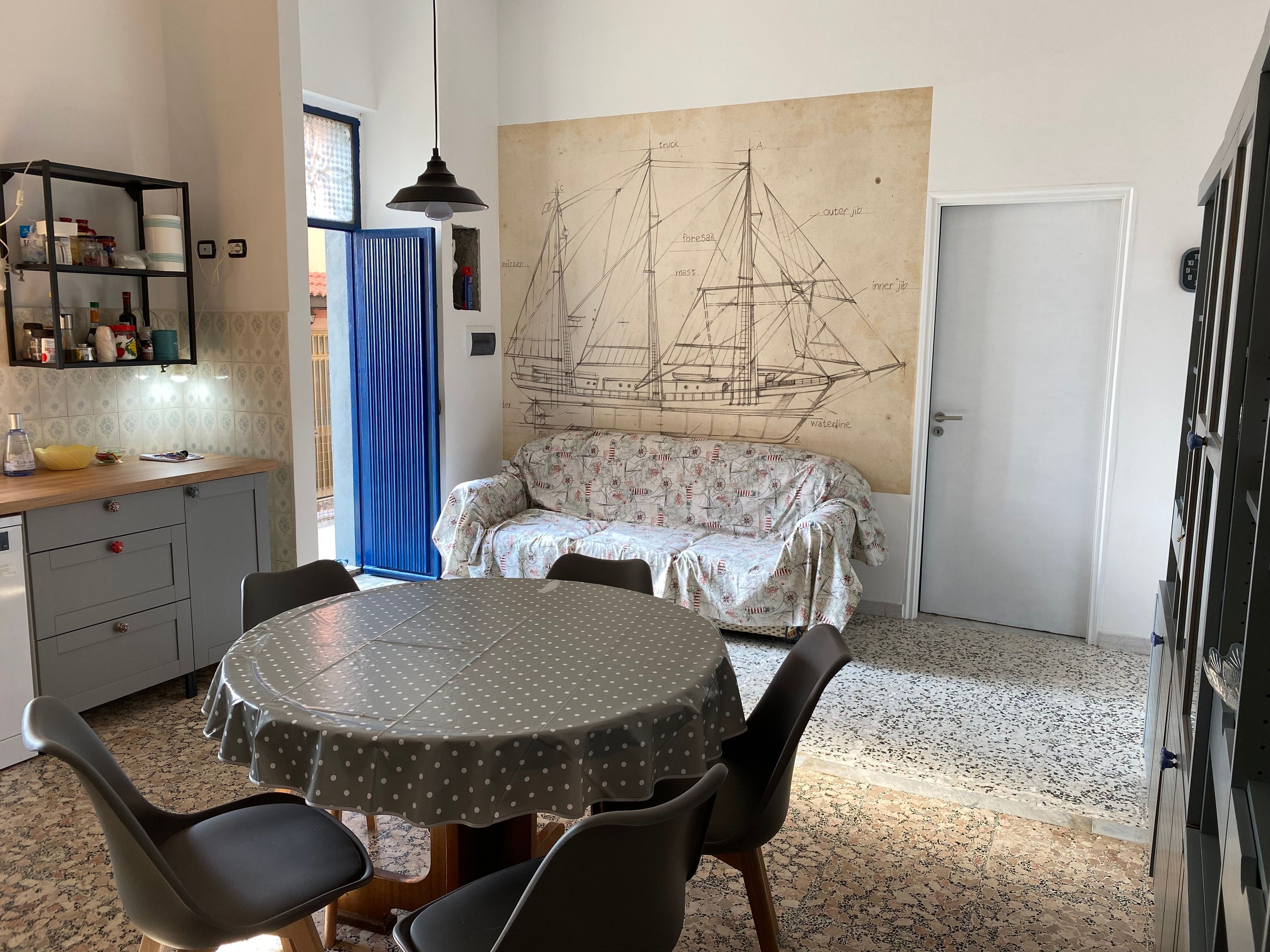 A dining area with a round table, chairs, a sofa, and a large ship-themed wall mural.