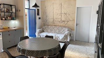 A dining area with a round table, chairs, a sofa, and a large ship-themed wall mural.