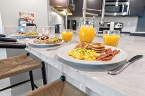 Ein Frühstückstisch mit Rührei, Speck, Pfannkuchen und Toast, dazu Orangensaft.