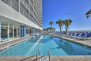 Ein Swimmingpool mit Liegestühlen und Palmen, neben einem Hotelgebäude mit Balkonen.