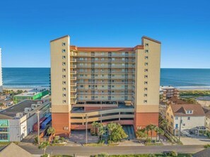 A multi-story hotel with a parking garage, located near a beach with the ocean in the background. - Malibu Pointe 1001 -I/O Pools-Lazy River-4BR/4BA (North Myrtle Beach)