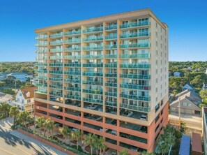 A multi-story hotel with a modern design, featuring balconies on each floor and a parking area below. - Malibu Pointe 1001 -I/O Pools-Lazy River-4BR/4BA (North Myrtle Beach)