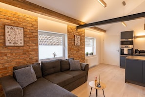 A modern living room with a sectional sofa, a small round table, and a kitchen area with built-in appliances.
