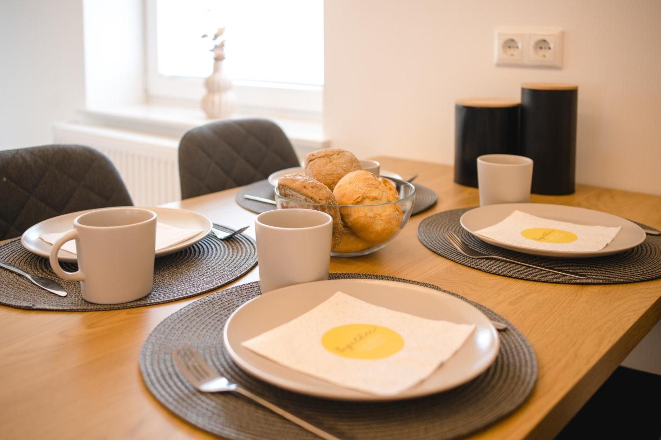 A breakfast setup with plates, mugs, and a bowl of pastries on a wooden table.