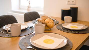 A breakfast setup with plates, mugs, and a bowl of pastries on a wooden table.