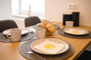 Una mesa de madera con platos, tazas y un bol de pasteles para el desayuno.