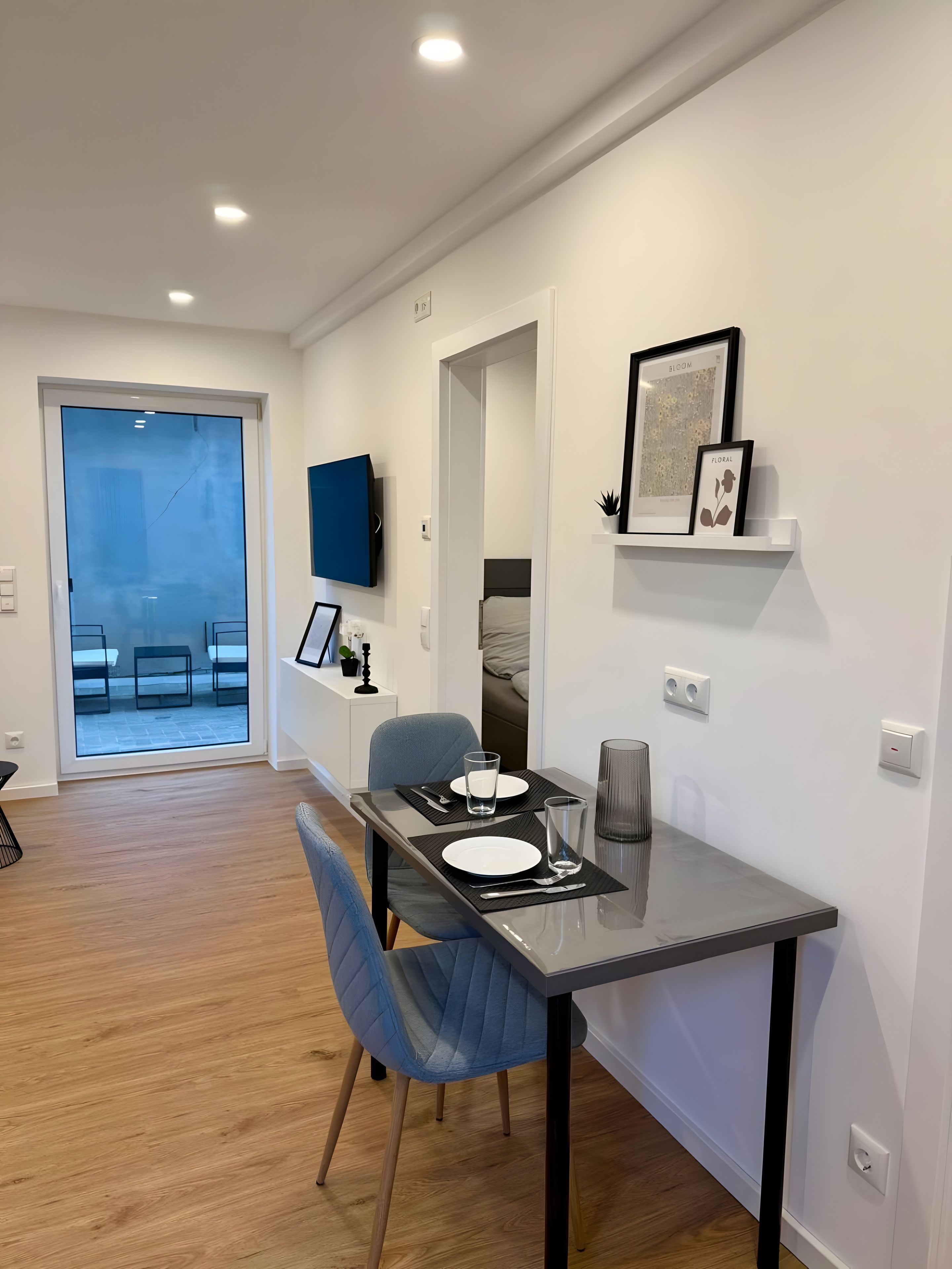 Un'area pranzo moderna con tavolo in vetro, sedie blu e vista su un patio esterno.