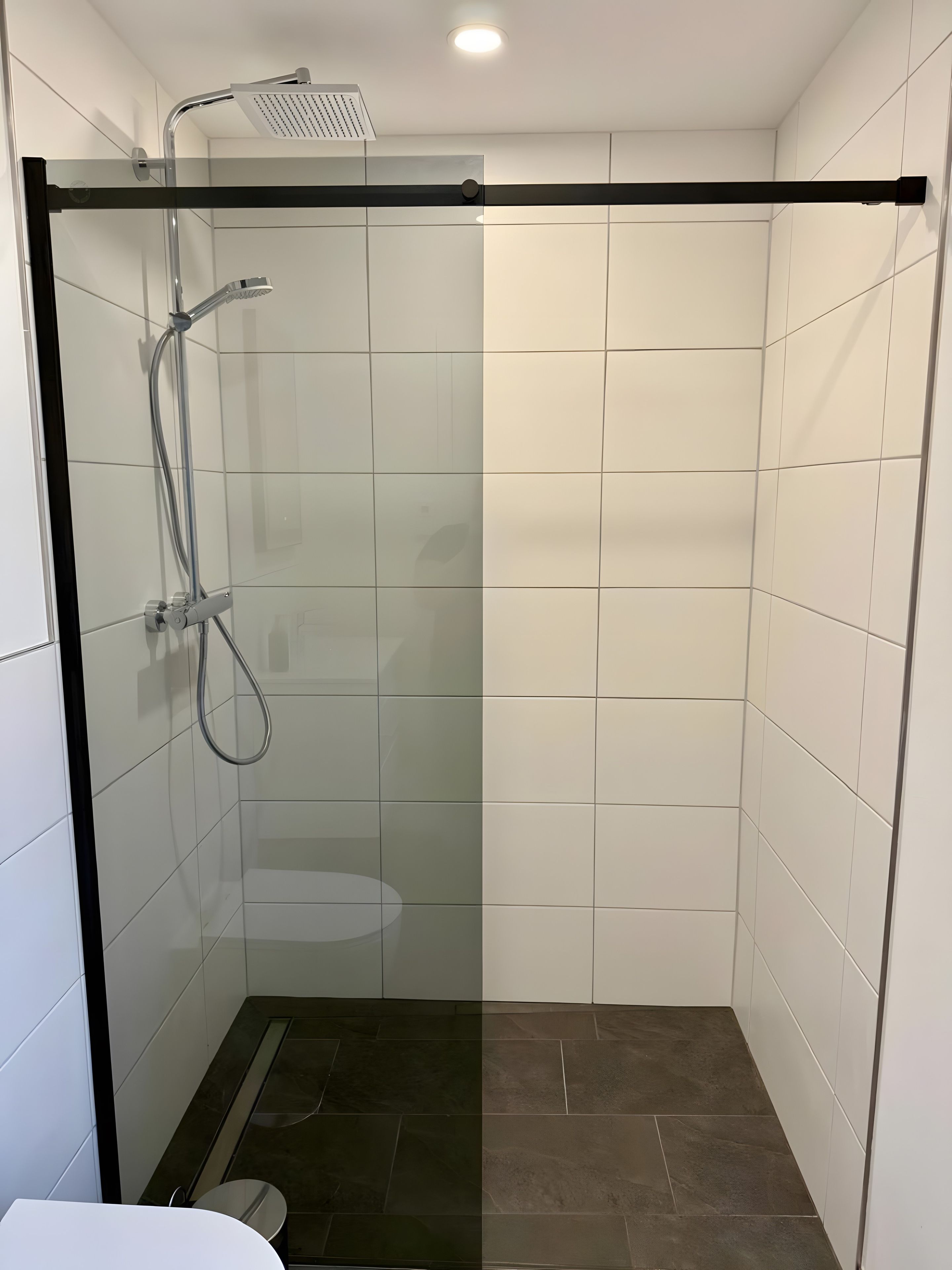 A modern shower enclosure with a glass door, a handheld showerhead, and a wall-mounted faucet.