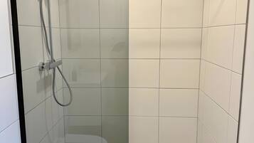 A modern shower enclosure with a glass door, a handheld showerhead, and a wall-mounted faucet.