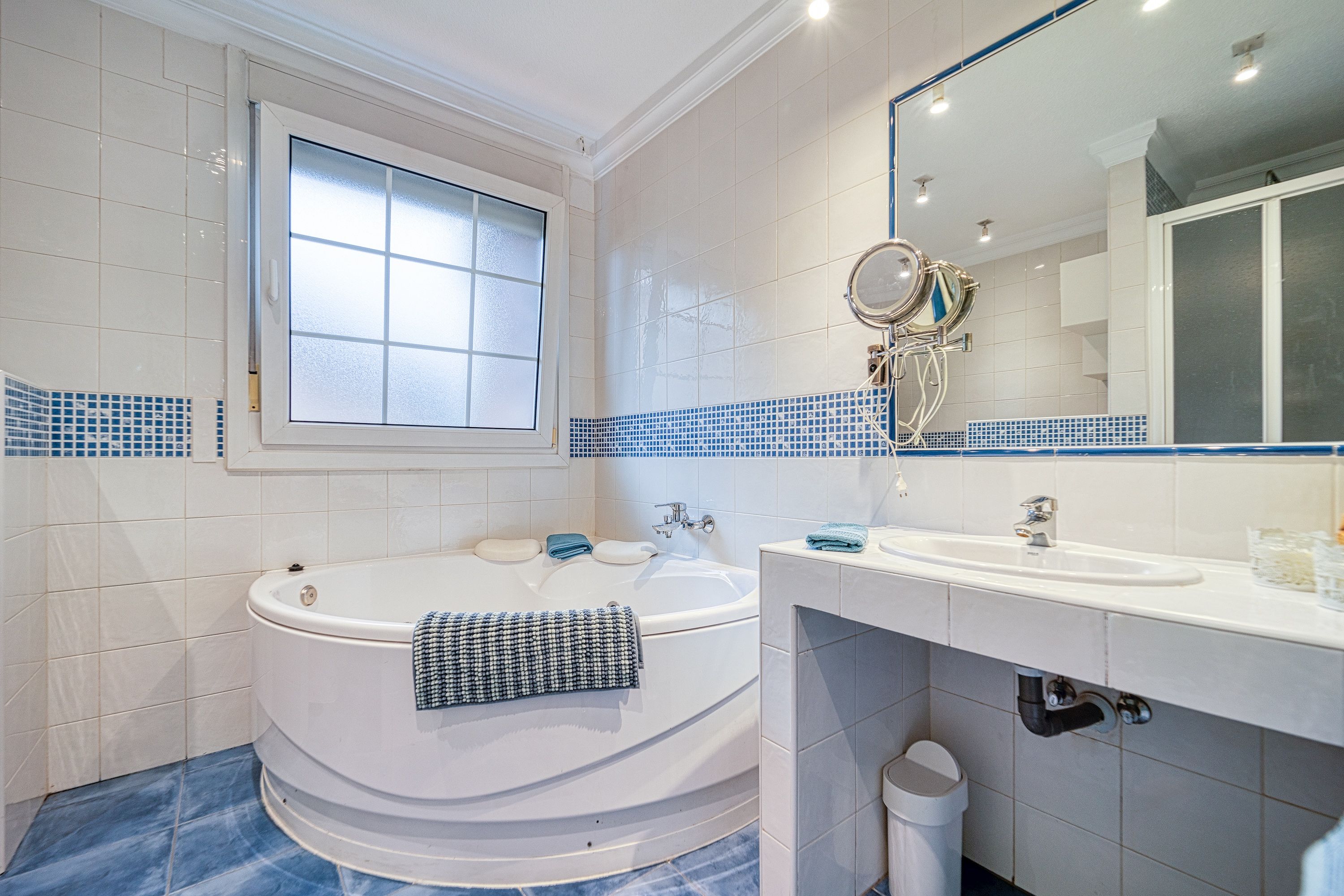 A bathroom with a bathtub, a sink, a mirror, and a window.