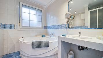 A bathroom with a bathtub, a sink, a mirror, and a window.