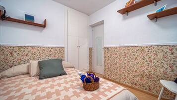 Un dormitorio con cama, almohadas, una mesita de noche, estante en la pared y una puerta.