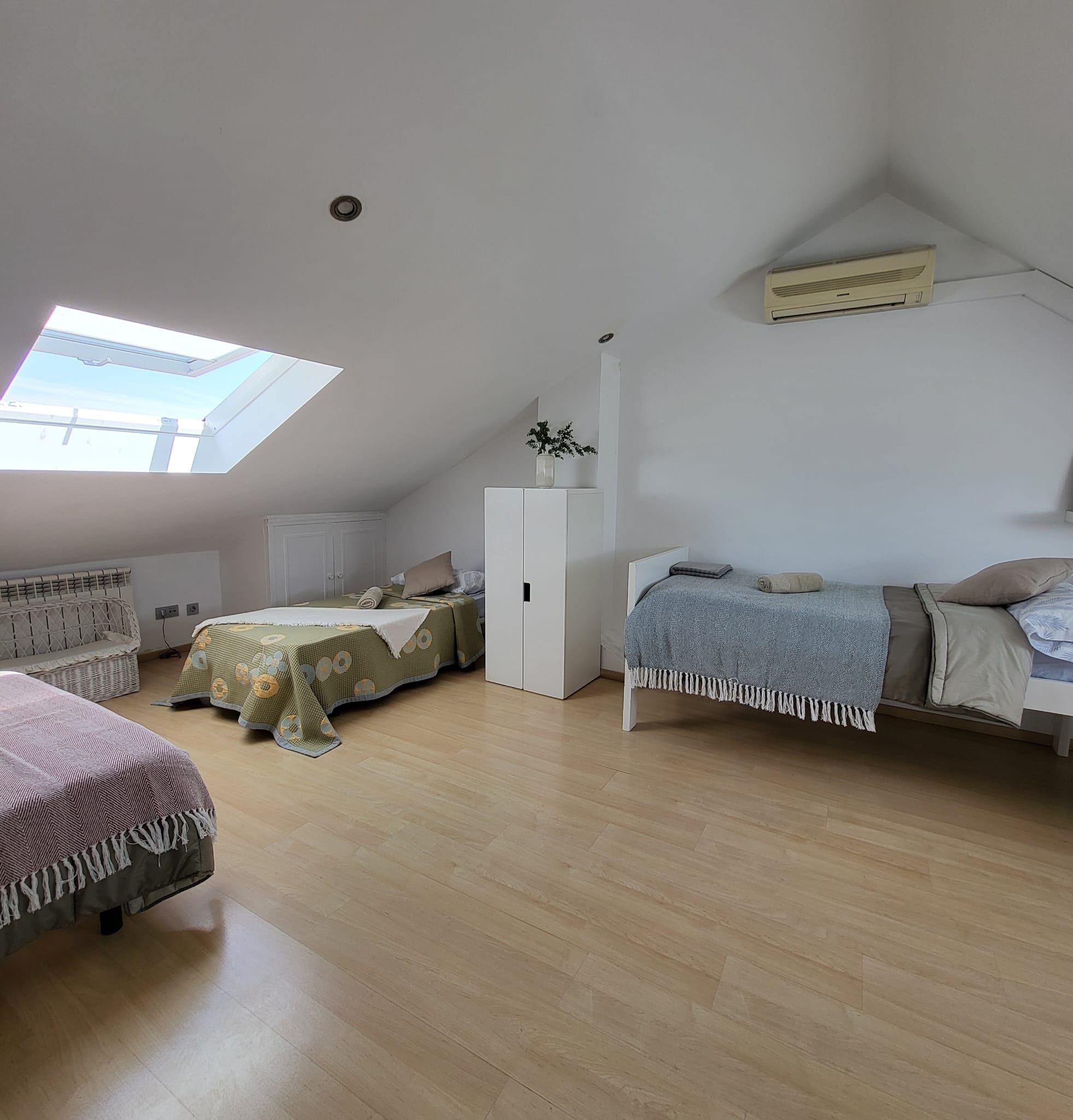 Une chambre avec deux lits, un puits de lumière, une armoire blanche et un ventilateur de plafond.