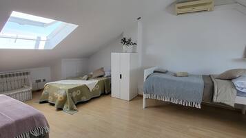 Une chambre avec deux lits, un puits de lumière, une armoire blanche et un ventilateur de plafond.