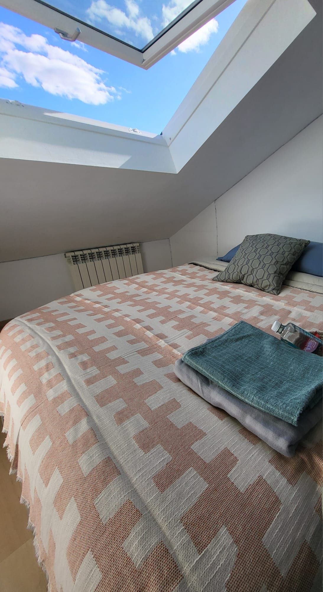 Un dormitorio con tragaluz, colcha estampada y radiador.
