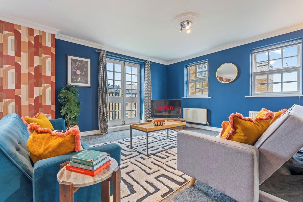 Ein Wohnzimmer mit blauen Wänden, einem Fernseher, zwei Sofas mit Kissen, einem Couchtisch und einem gemusterten Teppich.