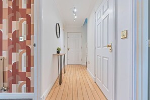 A hallway with a patterned wall, a door, a small table with a plant, and a light fixture on the ceiling. - Artist Abode in York (York)