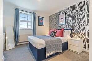 A bedroom with a bed, a nightstand, a dresser, a window with curtains, and a patterned wall. - Artist Abode in York (York)