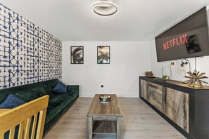 A modern living room with a green sofa, wooden coffee table, and a TV mounted on the wall. - Stylish 2-Bedroom Retreat in Southampton (Southampton)