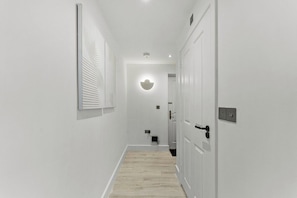 A hallway with a light-colored floor, white walls, and a door with a handle. - Stylish 2-Bedroom Retreat in Southampton (Southampton)
