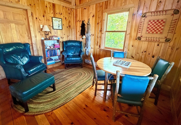 A wooden interior with a round table, blue chairs, a bookshelf, and a chessboard on the wall.