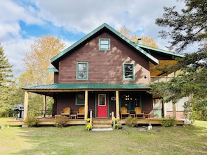 A wooden house with a porch, two windows, and a red door.