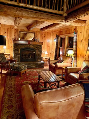 A cozy log cabin interior with a stone fireplace, leather furniture, and wooden walls.