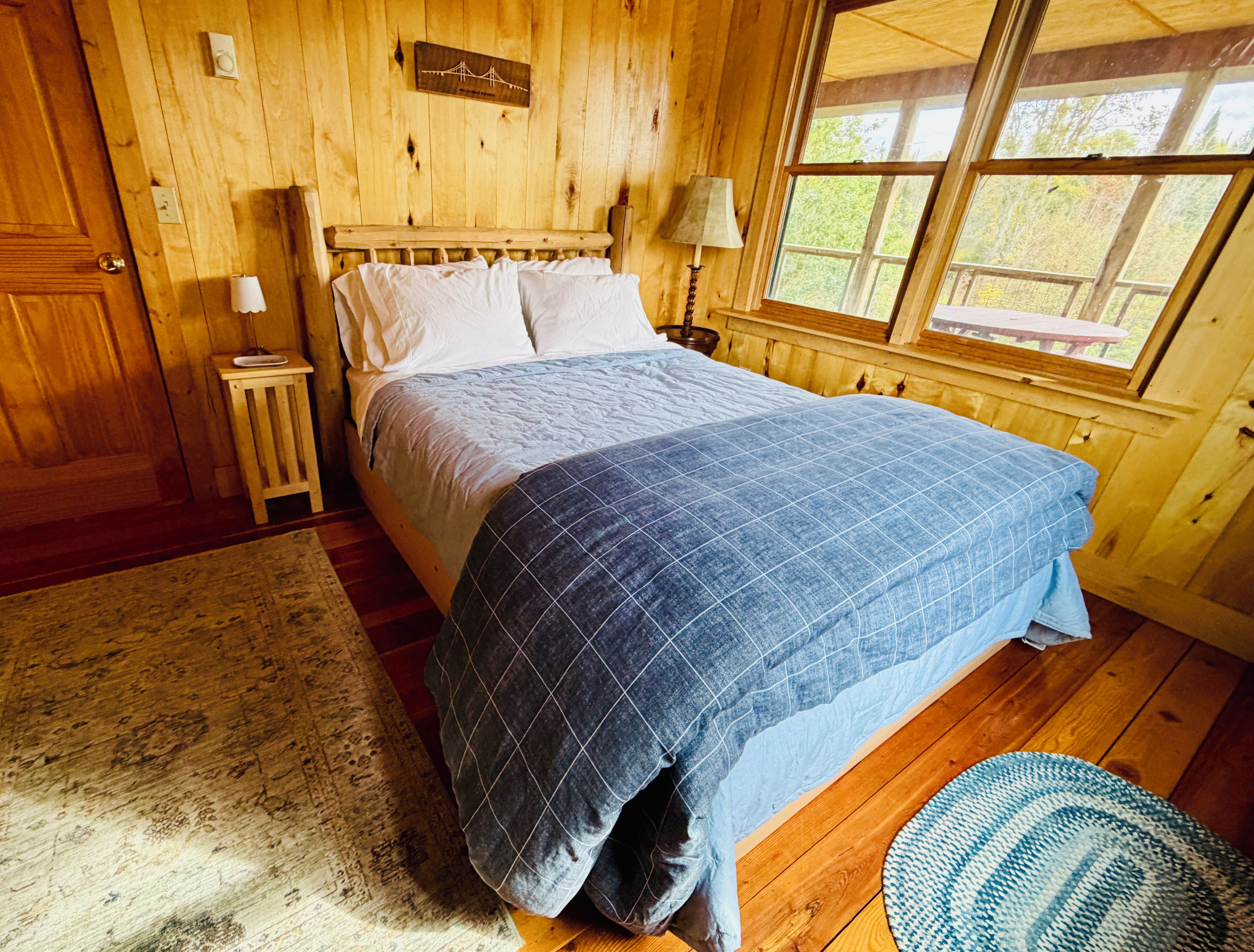 Une chambre à coucher dans un chalet en bois, avec un lit, une table de chevet, une lampe et une fenêtre donnant sur la forêt.