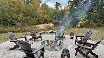 Un aménagement circulaire avec des sièges disposés en cercle autour d’un foyer, et des fauteuils Adirondack placés tout autour.